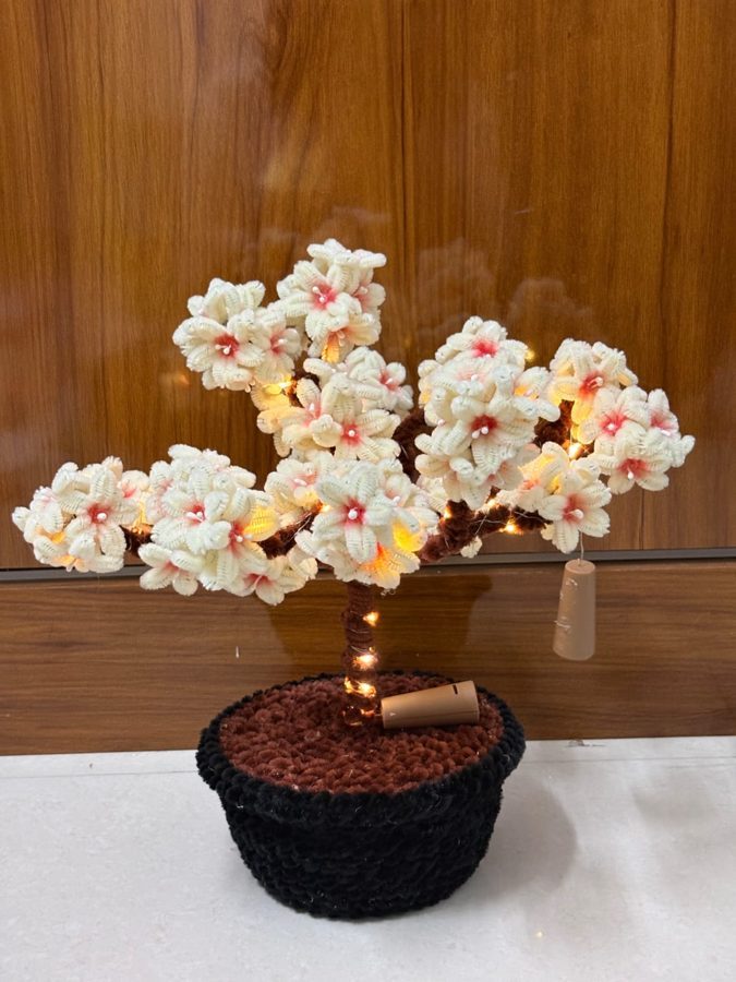 Blossom Glow Bonsai. Handcrafted cherry blossom bonsai made from soft chenille wire, with cream-and-pink flowers and warm LED fairy lights. Set in a black knitted pot. A lasting decor piece for any desk or shelf.