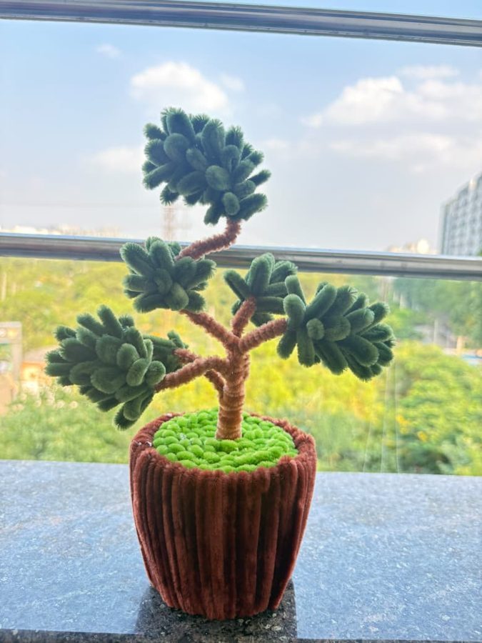 Evergreen Bonsai. Handcrafted bonsai tree made from soft chenille wire, with layered green foliage on brown branches. Set in a brown knitted pot with a lush green moss top. A calm, long-lasting piece for any desk or s…