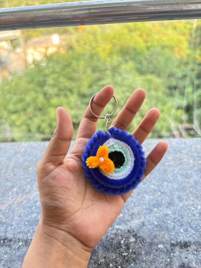 Evil Eye Blossom Keychain. Handcrafted evil eye keychain made from soft chenille wire, with a blue, white, and aqua eye design and a small orange flower with a pearl center. A cute, protective charm for keys or bags.