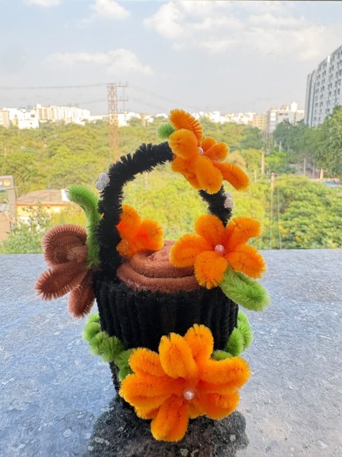 Marigold Mini Basket. Handcrafted mini flower basket made from soft chenille wire, with orange blossoms, pearl centers, and green leaves. Finished with a black handle and a knitted base. A bright little gift for any d…