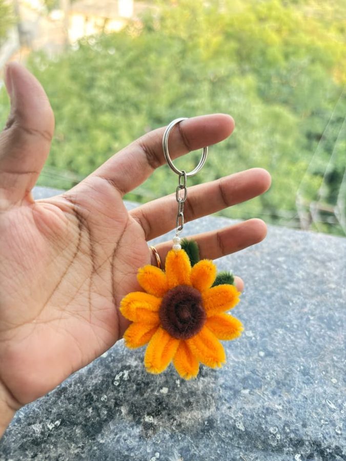 A sunflower chenille keychain with a pearl bead, held in a hand.